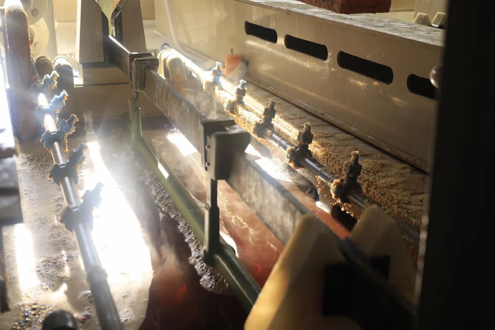 Close-up of the Ecosophia production process showing heated industrial treatment equipment with steam, spray nozzles and conveyor handling inside the manufacturing line